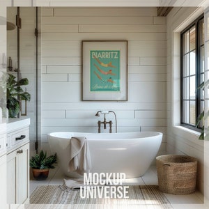 May include: A white freestanding bathtub with a towel draped over the edge, a small potted plant, and a woven basket in a bathroom with white shiplap walls, a framed poster with the text "BIARRITZ Bains de Mer", and a window with black trim.