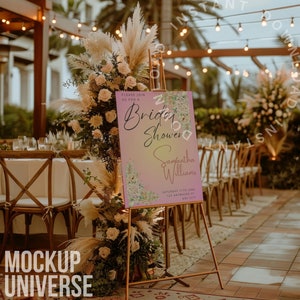 May include: A pink and white bridal shower sign with a floral design and the text "Please join us for a Bridal Shower Samantha Williams Saturday 11th June 123 Somewhere City". The sign is on a gold easel in front of a table with chairs and a floral arrangement.