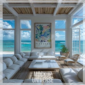Könnte beinhalten: Ein weißes, geteiltes Sofa mit weißen Kissen steht in einem Wohnzimmer mit großen Fenstern, die auf einen Strand blicken. Ein Couchtisch mit Büchern und einem gerahmten Gemälde einer farbenfrohen abstrakten Landschaft mit dem Text "MATISSE" steht vor dem Sofa. Zwei Korbstühle stehen im Vordergrund.