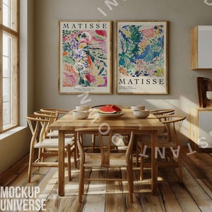 May include: Two framed art prints of colorful abstract paintings by Matisse, hanging on a light beige wall above a wooden dining table with six chairs. The table is set with a bowl of fruit, plates, and glasses.