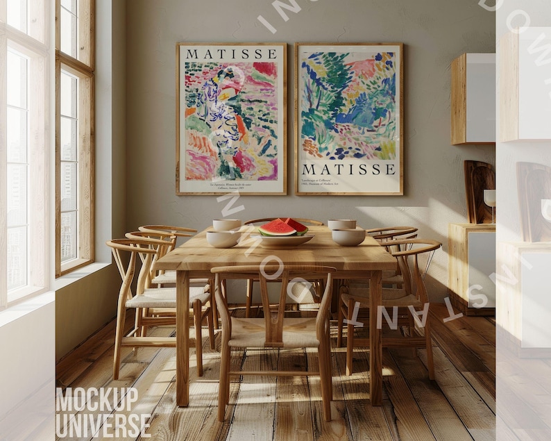 May include: Two framed art prints of colorful abstract paintings by Matisse, hanging on a light beige wall above a wooden dining table with six chairs. The table is set with a bowl of fruit, plates, and glasses.