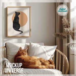 Könnte beinhalten: Ein digitaler Download eines minimalistischen Kunstdrucks mit einer schwarzen Katze, die vor einem beigefarbenen Kreis sitzt. Der Druck ist gerahmt und hängt an einer Wand in einem Wohnzimmer. Eine orangefarbene Katze schläft auf einem Sofa im Vordergrund.