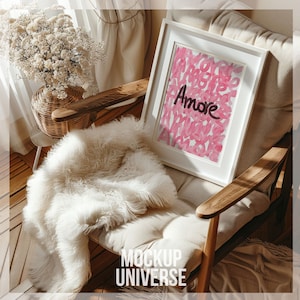Puede incluir: Una imagen enmarcada en blanco con un diseño abstracto rosa y blanco y la palabra "Amore" en letras negras. La imagen está sentada en una silla de madera con una manta de piel sintética blanca.