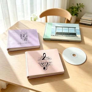 May include: A light purple photo album with a hand gesture and floral graphic, a light pink photo album with a treble clef and musical notes, a photo album with a beach bus stop image, and a blank silver CD, all featuring the text Willson's Collection.