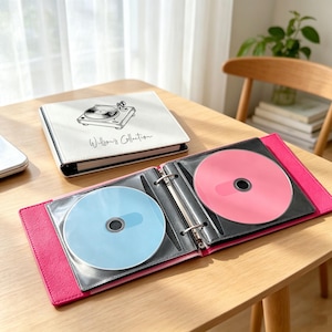 May include: A white binder with a black line drawing of a record player and the text "Willson's Collection" on the cover, alongside an open pink binder containing a light blue disc on the left and a solid pink disc on the right side.