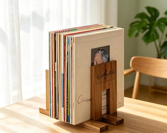 May include: A wooden vinyl record storage stand holding a collection of records. The stand features a dark brown wood grain finish and a laser-engraved design on the front panel showing a musical treble clef, a heartbeat line, and the text Wilson's Collection.