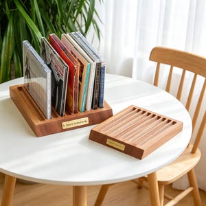 May include: Two rectangular wooden storage racks for compact discs, each featuring multiple parallel grooves for upright display. A small brass-colored metal plate is attached to the front of each rack, engraved with the text "Anna's Collection".