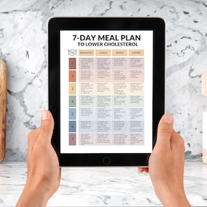 Op de afbeelding: Een tablet met een 7-daags maaltijdplan om cholesterol te verlagen. Het plan is georganiseerd per dag en maaltijd, met kolommen voor ontbijt, lunch, snack en diner. De tablet wordt door twee handen vastgehouden.