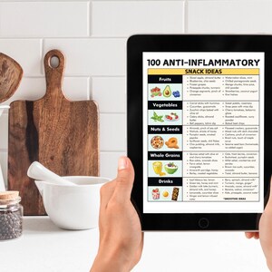 May include: A digital tablet displaying a list of 100 anti-inflammatory snack ideas, categorized by food groups: fruits, vegetables, nuts & seeds, whole grains, and drinks. The list includes specific examples of each food group, such as blueberries, zucchini, almonds, quinoa, and green tea.