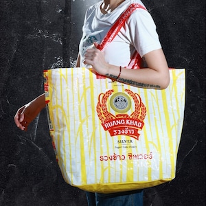 May include: A yellow and white tote bag with a red logo that says "RUANG KHAO" and "SILVER Sugar Cane Honey". The bag has a pattern of vertical white lines on a yellow background.