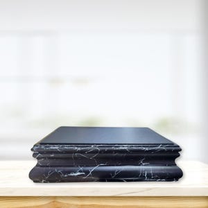 May include: Black marble pedestal with a smooth, flat top surface. The pedestal has a decorative, layered design with a rounded edge.