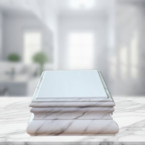 May include: A white marble pedestal with a smooth, flat top surface. The pedestal has a decorative, curved base.