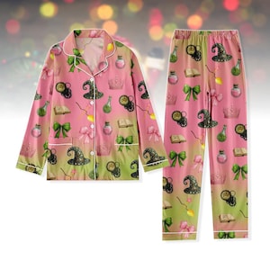 May include: A pink pyjama set featuring a pattern of witch hats, potion bottles, books, bows, and crowns. The long-sleeved top has white trim and buttons. The pyjama trousers have a matching pattern and a comfortable fit.