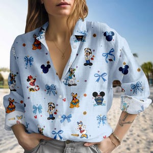 May include: Light blue button-down shirt featuring a repeating pattern of Disney characters, including Mickey Mouse, Minnie Mouse, Goofy, and Donald Duck. The shirt also has blue bows and nautical elements. The shirt is made of a lightweight fabric.