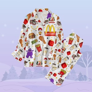 Könnte beinhalten: Weißer Schlafanzug mit einem sich wiederholenden Muster aus McDonald's-Essen und -Charakteren, darunter Pommes, Chicken Nuggets, Hamburger und das Maskottchen Grimace. Der Schlafanzug hat ein Oberteil mit Knöpfen und eine lange Hose.