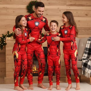 May include: A family of five wearing matching red and gold Iron Man pajamas. The pajamas feature a detailed design mimicking the Iron Man suit, with a central chest emblem. The group is smiling and standing in front of a fireplace.
