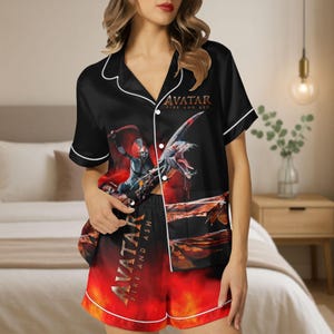 May include: Black pajama set with white trim featuring a graphic from "Avatar: Fire and Ash". The short-sleeved top and shorts display a fiery red and black design with characters and text. The set is made of a silky material.