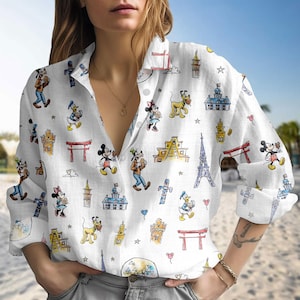May include: White button-down shirt featuring a repeating pattern of cartoon characters and landmarks. The design includes Mickey Mouse, Donald Duck, Minnie Mouse, Goofy, and Pluto, along with the Eiffel Tower and other architectural elements.