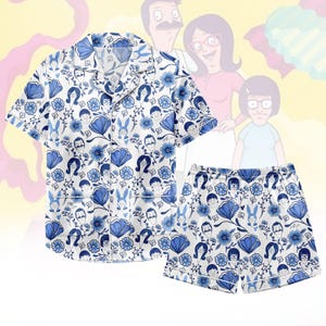 Puede incluir: Conjunto de pijama blanco y azul con estampado floral y de personajes. La camiseta de manga corta y los pantalones cortos tienen un diseño repetido de flores azules, caras de dibujos animados y figuras de conejos. El conjunto tiene ribetes blancos.