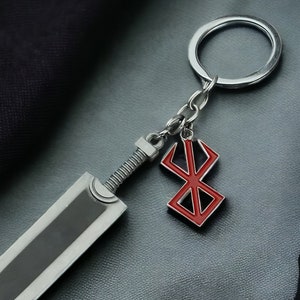 May include: A silver-colored sword keychain with a black blade and a red and black charm. The keychain has a silver ring and a detailed handle. The charm is a red and black symbol.