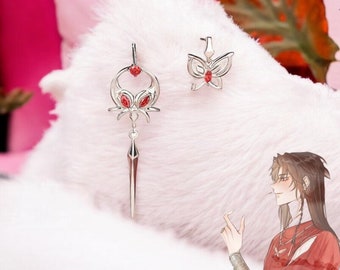 May include: A pair of silver earrings with red gemstone accents. One earring features a butterfly design, while the other has a more intricate design with a pointed drop.