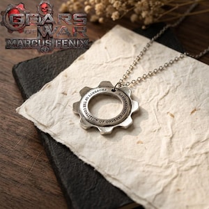May include: A silver-toned metal pendant shaped like a gear on a matching chain. The pendant features the engraved text Property of the Coalition of Ordered Governments. The image also displays the Gears of War Marcus Fenix logo in the corner.