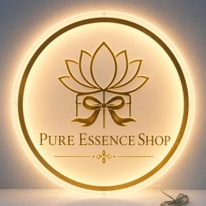 May include: A round, illuminated sign with a gold lotus flower and bow design. The text "Pure Essence Shop" is displayed below the floral graphic. The sign has a warm, inviting glow.
