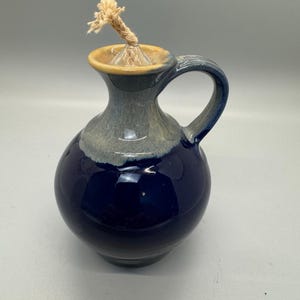 May include: A blue and white ceramic oil lamp with a wick and a handle. The lamp has a glazed finish.