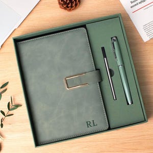 以下が含まれることがあります： ゴールドの長方形の留め具とRLのイニシャルが刻印されたセージグリーンのノートブック。同色のギフトボックスに収められ、セージグリーンのペンと細い金属製の替え芯がセットになったステーショナリーセットです。