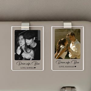May include: Two clear acrylic car visor photo holders with metal clips. Each holder contains a photograph of a couple. The text "Drive safe, Bae" and a name are printed on each holder.