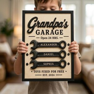May include: A framed sign reading "Grandpa's Garage" in a 3D style. Below the text are three wrench designs with the names "Alexander", "Daniel", and "Sophia". The sign also reads "Open 24 HRS." and "TOYS FIXED FOR FREE - EST. 2024".