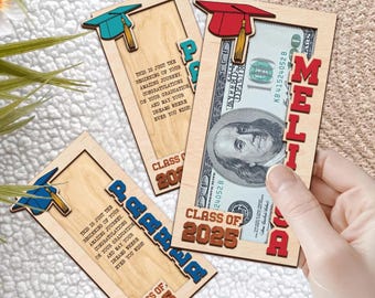 Puede incluir: Tres tarjetas de graduación de madera con una ranura para dinero. Cada tarjeta tiene un diseño de gorro de graduación, el texto "Clase de 2025" y un nombre personalizado. Las tarjetas están sobre una superficie blanca.