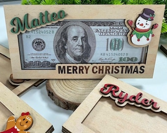 Könnte beinhalten: Zwei hölzerne Weihnachtsgeschenkrahmen mit den personalisierten Namen "Matteo" und "Ryder". Der Matteo-Rahmen zeigt einen 100-Euro-Schein mit einem Porträt von Benjamin Franklin und dem Text "Frohe Weihnachten". Der Ryder-Rahmen hat einen leeren Platz für ein Foto.
