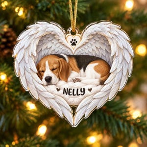 May include: A heart-shaped ornament featuring a sleeping beagle puppy surrounded by white angel wings. A small heart with a black paw print sits at the top. The name NELLY is printed in black letters below the puppy, flanked by two small hearts.