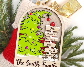 May include: A wooden Christmas ornament featuring a green cartoon Christmas tree with a whimsical design. The ornament has a white background with a snow-covered base and a red ribbon. The ornament also includes a sign with the names "Don, Madison, Melissa, Tobi, Luna, Spooky" and the year "2024". The text "The Smith Family" is printed at the bottom of the ornament.