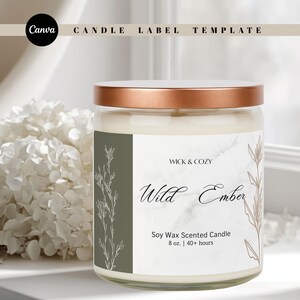 May include: A glass jar candle with a copper lid, labelled "Wild Ember." The label features botanical illustrations and the text "Soy Wax Scented Candle, 227g | 40+ hours." The background includes white flowers and a window.