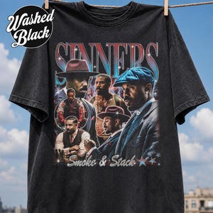 Peut inclure: Un t-shirt à manches courtes noir délavé avec une impression graphique portant le texte "SINNERS" et "Smoke & Stack". Le motif comprend plusieurs portraits d'hommes en chapeaux et costumes, agrémentés d'étoiles scintillantes et d'un dégradé rouge et bleu.