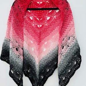 Pode incluir: Um xale de crochê degradê vermelho, rosa e preto com um padrão de renda. O xale está pendurado em um cabide preto. O texto "RED/BLACK" é visível no canto superior direito da imagem.