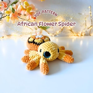 May include: A crochet spider toy made of soft yellow and orange yarn with large blue eyes. The text PDF PATTERN African Flower Spider is displayed above the toy, which features a patterned back and eight segmented legs.