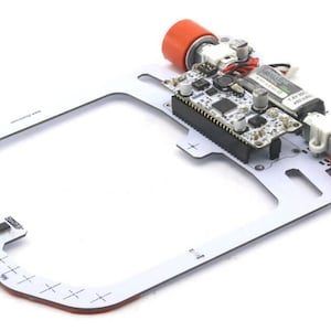 Op de afbeelding: Een wit robotchassis met een printplaat en twee rode wielen. De printplaat heeft een zwarte chip en een groen onderdeel met de tekst "1.6V 1000 400 Ohm".