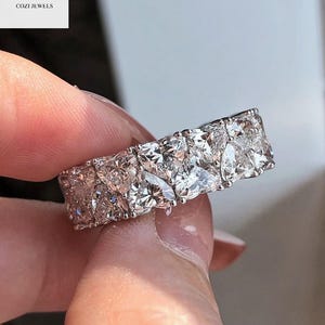 May include: A silver band ring with a row of large, clear, round, and square-shaped diamonds.