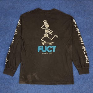 May include: Black long-sleeve t-shirt with a skeleton skateboarding graphic and the text "FUCT A TOAST TO DEATH" on the back. The sleeves have a repeating skeleton graphic.