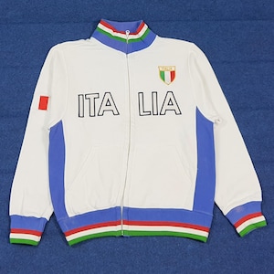 May include: White zip-up track jacket with blue and green accents. The jacket features the word "ITALIA" in black block letters, an Italian flag patch, and a small Italian flag on the left sleeve.
