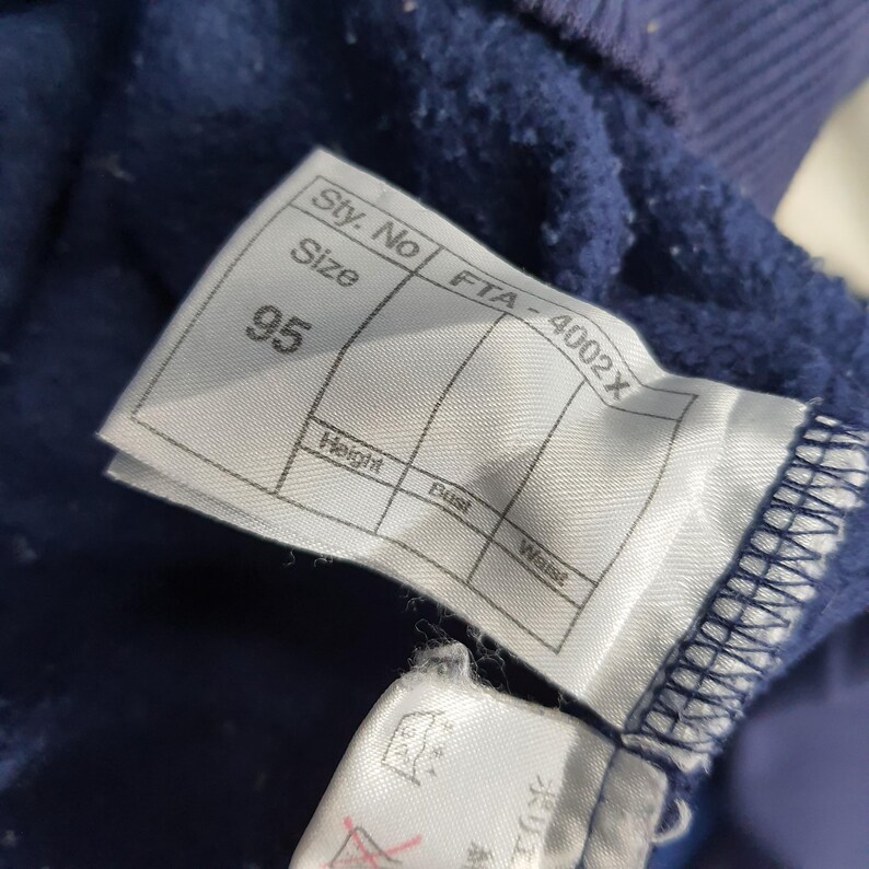 Puede incluir: Primer plano de una etiqueta de prenda azul marino con el n&uacute;mero 95 impreso. La etiqueta tambi&eacute;n incluye el texto "Sty. No", "Size", "Height", "Bust" y "Waist". La etiqueta est&aacute; adherida a una tela azul marino.