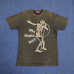 Puede incluir: Camiseta negra con un esqueleto sosteniendo un micrófono y el texto "Who laughs last?" impreso en ella.