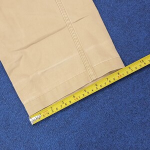 May include: Tan-colored fabric with a seam detail is measured with a yellow tape measure. The tape measure shows a measurement of approximately 3 inches. The fabric appears to be part of a pair of pants.