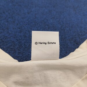 Puede incluir: Etiqueta de tela blanca con texto negro que dice "&copy; Haring Estate".