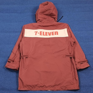 Puede incluir: Chaqueta con capucha de color granate con el logotipo de 7-Eleven en letras rojas sobre una franja blanca en la espalda. La chaqueta tiene capucha con cordón, dos bolsillos y puños ajustables. Fabricada con un material ligero.
