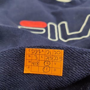 Puede incluir: Sudadera azul marino con el logo de FILA en blanco y rojo. Una peque&ntilde;a etiqueta naranja con texto negro est&aacute; adherida a la prenda. La sudadera est&aacute; hecha de un material suave y c&oacute;modo.