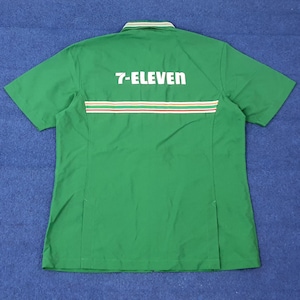 Puede incluir: Camisa verde de manga corta con el texto "7-ELEVEN" en blanco. La camisa tiene un cuello con rayas verdes y blancas y una franja horizontal roja, blanca y amarilla en la espalda. Uniforme.